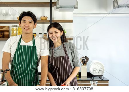 Portrait Of Cute Happy Couple In Aporn Jposting To Prepare Breakfast Decorated With Salad And Orange