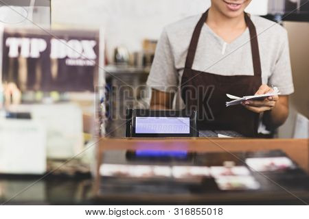 Female Cashier Operating Cash Register With Order In Her Hand In Cafe.