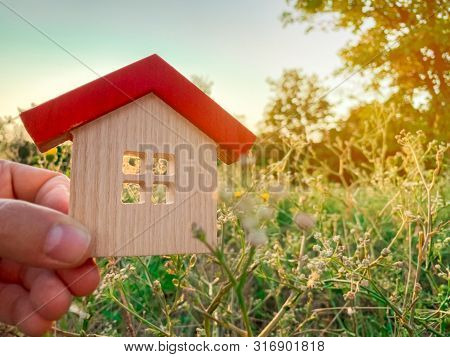 Miniature Wooden House In The Hands Of A Man Outdoors. Real Estate Concept. Eco-friendly Home. Buyin