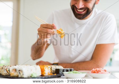 Handsome man smiling happy enjoying eating fresh colorful asian sushi using chopsticks