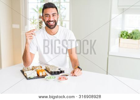 Handsome hispanic man eating asian sushi using chopsticks with a happy face standing and smiling with a confident smile showing teeth