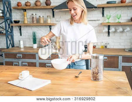 Close Up Smiling Young Woman In Kitchen Pours Milk In Dep Plate With Corn Flakes. Pretty Girl Has A 