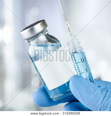 Healthcare concept with a hand in blue medical gloves holding a vaccine vial with blue liquid and black white label