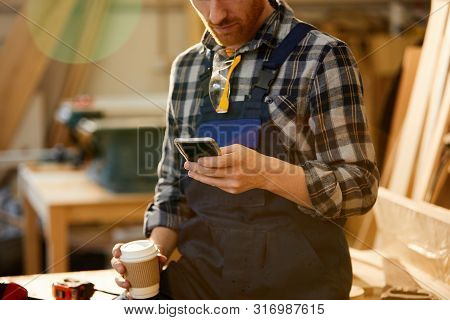 Mid Section Portrait Of Modern Carpenter Using Smartphone During Coffee Break In Joinery, Copy Space