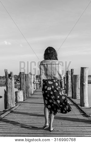 Black And White Picture Of Brunette Woman Walking At Wooden U Bein Bridge, Which Is A Touristic Attr