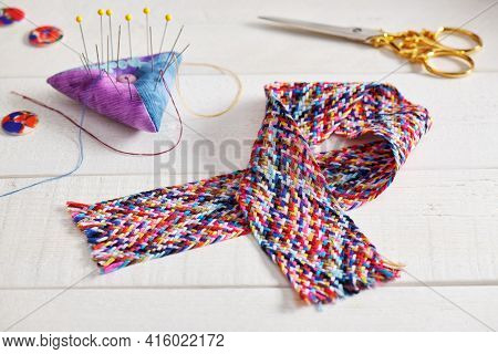 A Braid Of Multi Colored Sewing Threads, Pincushion, Scissors, Buttons Lying On A White Surface