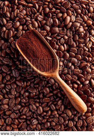 Wood scoop with ground coffee on beans background