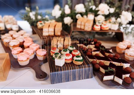 Candy Bar Decorated By Delicious Sweet Buffet With Cupcakes, Eclairs, Sweetness And Flowers, And Oth