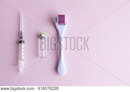 Dermaroller, Mesoscooter, Gold Microneedles, Hyaluronic Acid Ampoule And Syringe On A Pink Backgroun