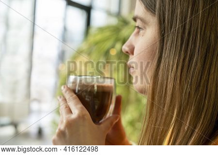 Young Pretty Caucasian Woman Holding Glass Cup Of Coffee Or Cocoa And Meditating Looking Out The Win