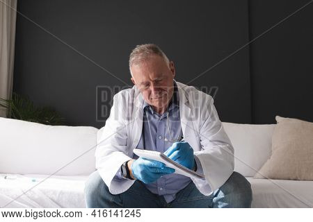 Caucasian senior male doctor making notes during consultation video call. telemedicine online during quarantine lockdown.
