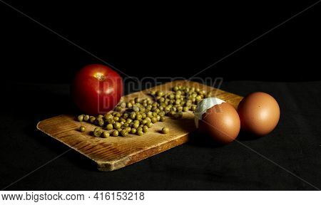 Two Eggs, Peas And A Tomato On A Wooden Board