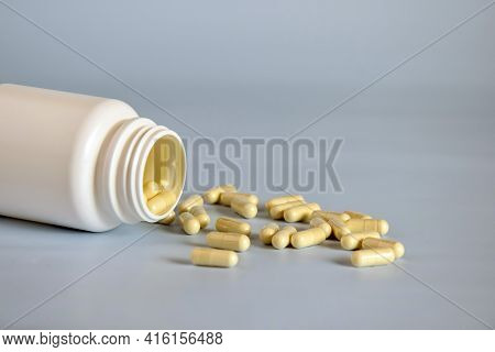 Natural Yellow Capsules With Medicinal Herb In Gelatin Shell, Pills In Open Upturned Plastic Jar. Al