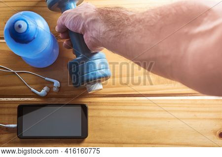 Fitness Equipment At Home, Top View Of Hand Holding Dumbbell, Water Bottle And Mobile Phone With Ear