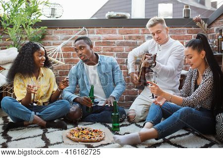 Happy Diverse Friends Sitting Together On Open Terrace With Tasty Pizza And Alcoholic Drinks. Young 