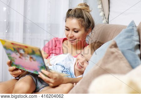 A Mother And Her Son Have Fun Together Reading A Book At Home On The Couch