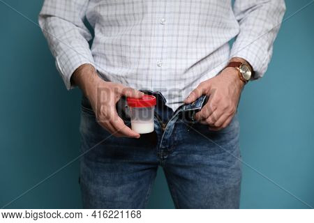 Donor With Unzipped Pants Holding Container Of Sperm On Turquoise Background, Closeup