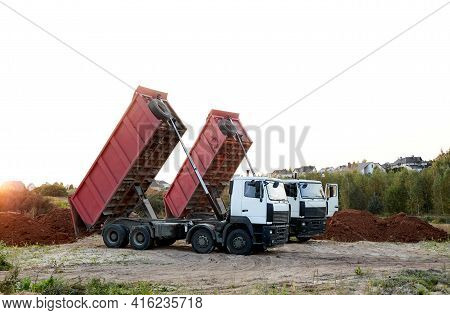 Two Red Dump Trucks Simultaneously Lifted The Bodies To Unload The Sand. Cargo Transportation Servic