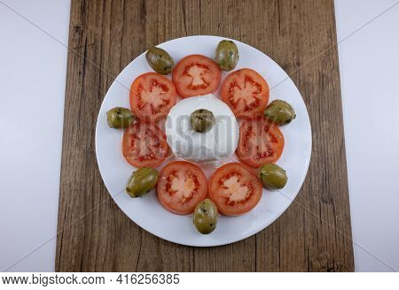 The Meal On A White Plate And Wooden Table Consists Of Sliced Tomatoes, Pitted Olives And Mozzarella