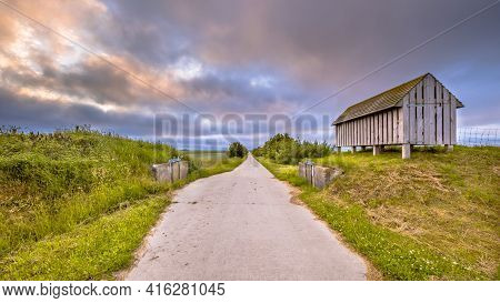 Road Passage Through Old Sea Dike At Sunset Under Beautiful Clouded Sky. Usquert, Groningen Province