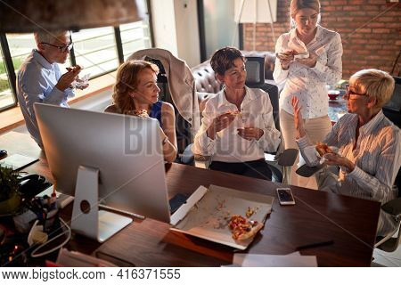 Group of cheerful business women are chatting while they eating a pizza at the break from work in a relaxed atmosphere at workplace. Business, office, job