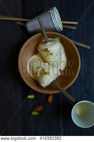 Delicious and authentic Kulfi - an Indian homemade ice cream served in an earthen bowl. Top view of Kulfi with moulds and sticks.
