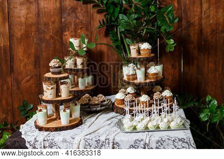 Candy Bar On Wooden Wedding Party With A Lot Of Different Candies, Cupcakes, Souffle And Cakes. Deco