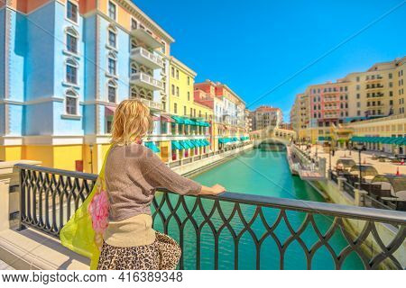 Blonde Woman On Balcony Looking Canals Of Venice In Doha Qatar. Caucasian Tourist Enjoys Qanat Quart