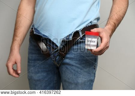 Donor With Unzipped Pants Holding Container Of Sperm On Beige Background, Closeup