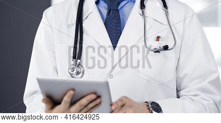 Unknown Male Doctor Iusing Tablet Computer In His Hands, While Standing In Clinic. Medicine Concept 