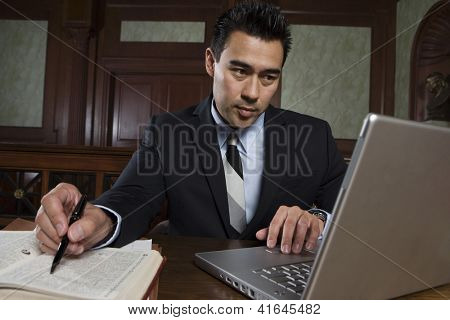 ทนายชายหนุ่มที่ใช้แล็ปท็อปในขณะที่กำลังเตรียมบันทึกย่อใน courtroom