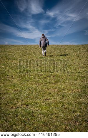 Woman Walking Alone Over The Grass Up The Hill In The Center Of The Picture In Sunny Weather And Spe