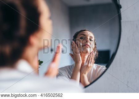 Woman Washes Her Face In Front Of The Mirror, Applying Foam To Her Cheeks