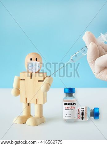 Simulation Of Syringe Vaccination Wooden Doll And A Vial For Protective Coronavirus With Blue Backdr