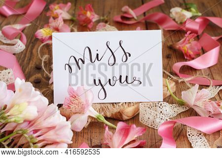 Miss You Handwritten Card On A Wooden Table Between Pink Flowers Close Up