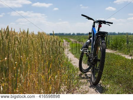 Bike Stands On The Road In The Field. A Mountain Bike Stands On A Field Path With Green Grass. Mount