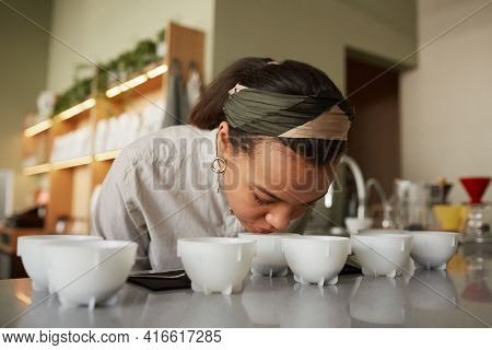 Portrait Of Mixed Race Young Woman Smelling Cofeee During Quality Assesment And Cupping Test In Cafe