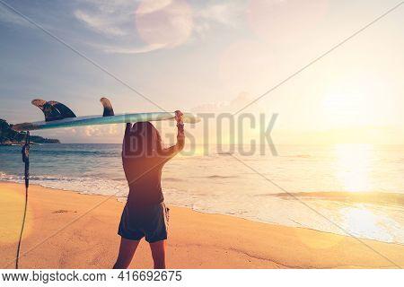 Woman Hold Surfboard Standing At Tropical Sunset Beach Background. Summer Vacation And Sport Adventr