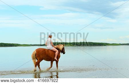One Caucasian Woman Is Riding Her Red Horse Along The Water In A Shallow Lagoon.