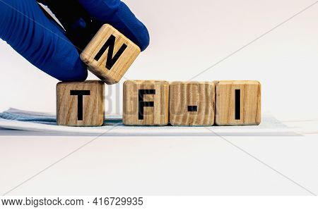 Text Tnf-i Made From Wooden Cubes. Hands In A Blue Glove.
