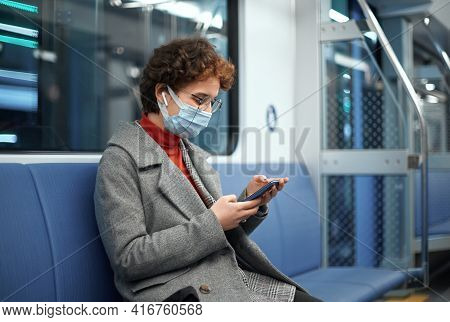 Woman In A Protective Mask Reading Correspondence Sitting In An Empty Subway Car.