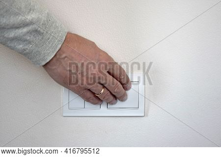 Male Hand Presses Button Of White Switch Mounted On Light Wall. Close-up. Selective Focus. Copy Spac