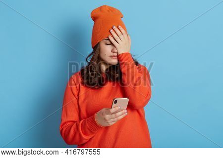 Frustrated Female Wearing Casual Clothing, Covering Face With Palm, Holding Phone In Hands, Forget S
