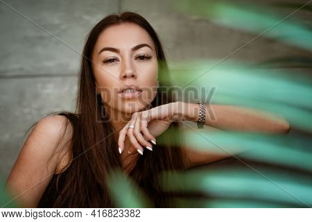 Beautiful Young Woman Closeup Portrait Through Green Leaves Of A Flower On A Gray Wall Background