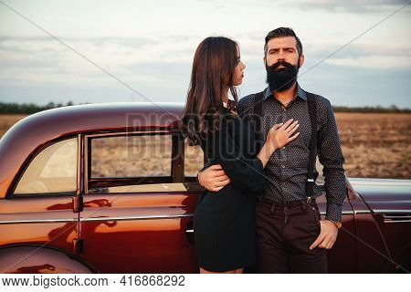 A Stylish Bearded Brunette In A Shirt And Trousers With Suspenders Hugs A Slender Young Girl With Lo