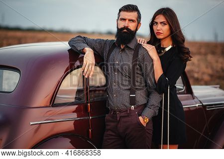 Stylish Bearded Brunette Man In A Shirt And Trousers With Suspenders Hugs A Slender Young Girl With 