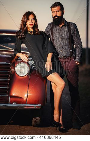Bearded Brunette Man In A Shirt And Trousers With Suspenders Hugs A Slender Young Girl With Long Hai