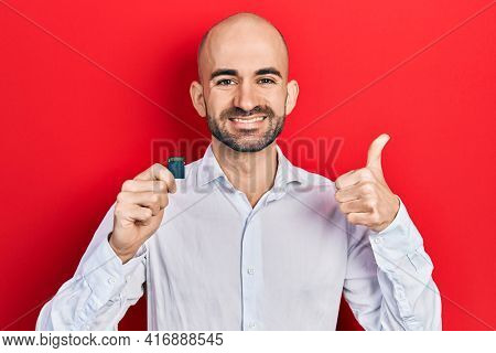 Young bald man holding sdxc card smiling happy and positive, thumb up doing excellent and approval sign 