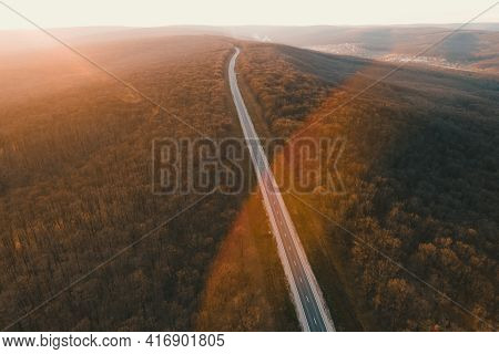Aerial Drone Overhead Of A Straight Road Through Leafless Forest Valley At Sunset. Highway Go Throug