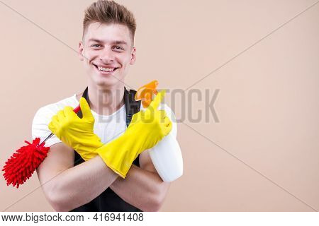 Young Smiling Househusband In Yellow Gloves, Apron Isolated On Beige Background. Houseworker Man Is 